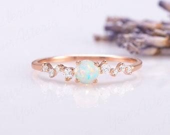 Può includere: Un delicato anello in oro rosa con una pietra di opale bianca e piccoli diamanti incastonati in un delicato motivo disperso.