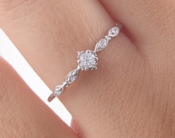 May include: A delicate silver ring with a small round diamond in the centre and smaller diamonds set in a curved design along the band.