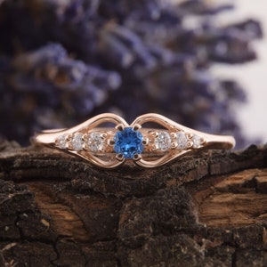 May include: A rose gold ring with a blue gemstone surrounded by smaller white gemstones. The ring has a delicate, openwork design.