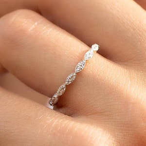 May include: A delicate silver band ring with a row of small, sparkling diamonds set in a marquise shape.