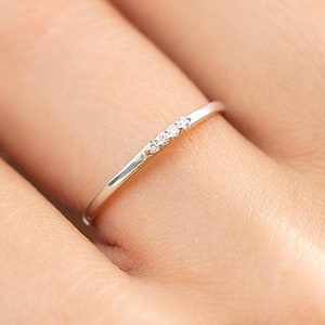 Op de afbeelding: Een delicate zilveren ring met drie kleine diamanten in een rij.