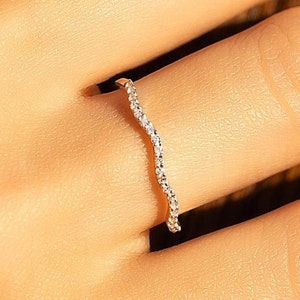 Op de afbeelding: Een delicate zilveren ring met een gebogen band van kleine glinsterende stenen.