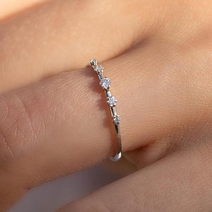 Può includere: Un delicato anello a fascia d'argento con cinque piccole pietre preziose trasparenti incastonate in fila.