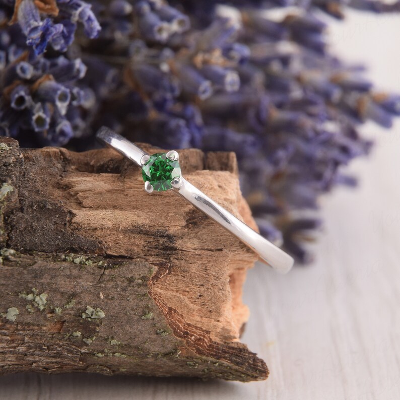 May include: A silver ring with a green gemstone set in a prong setting. The ring is resting on a piece of wood.