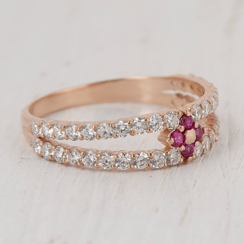 Puede incluir: Un anillo de oro rosa con una doble banda de peque&ntilde;as piedras transparentes y un grupo central de piedras rosas.
