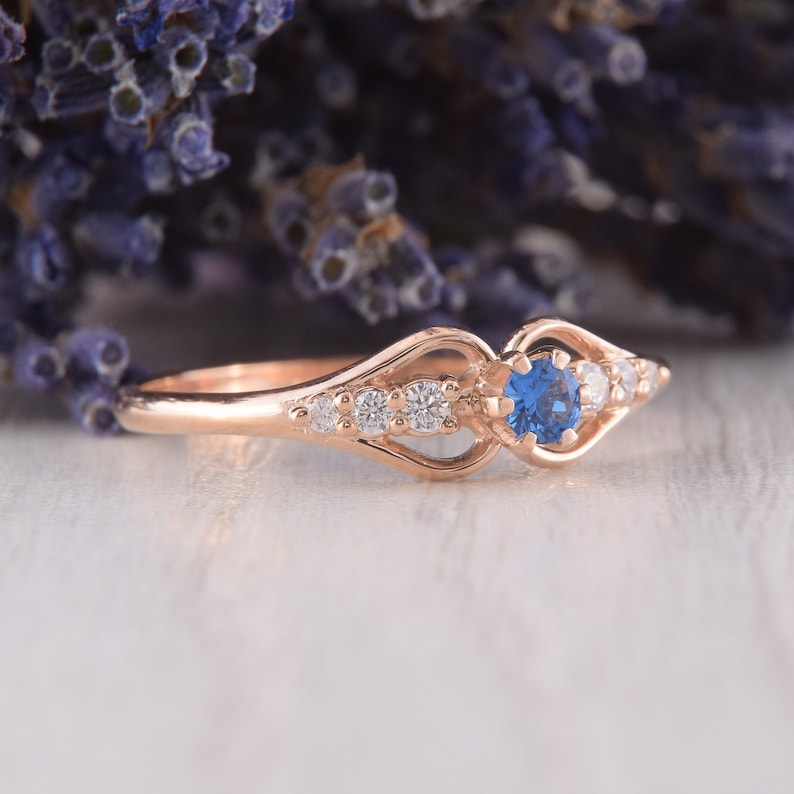 May include: A delicate rose gold ring with a blue sapphire center stone and smaller white diamonds set in a delicate, openwork design.