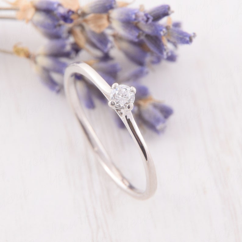 Pu&ograve; includere: Un delicato anello d'argento con una piccola gemma trasparente. L'anello &egrave; posto su uno sfondo sfocato di rametti di lavanda. Un gioiello semplice ed elegante, adatto a ogni occasione.