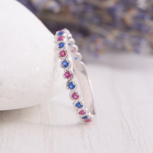以下が含まれることがあります： 波打つデザインのシルバーのバンドリング。交互に青い宝石とピンクの宝石が並んでいます。