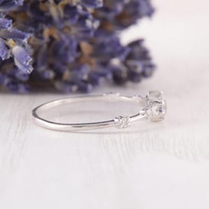 May include: A delicate silver ring with a small round gemstone and smaller accent stones. The ring is set on a white background.