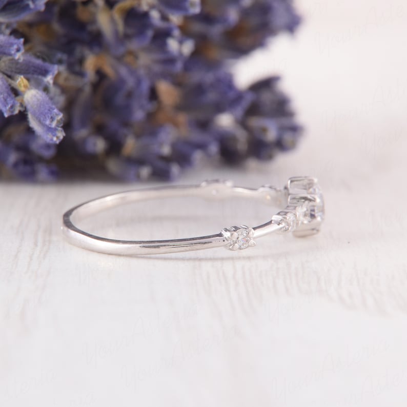 May include: A delicate silver ring with a small round gemstone and smaller accent stones. The ring is set on a white background.