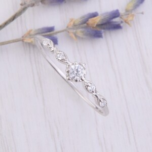 May include: A delicate silver ring with a small round diamond in the center and smaller diamonds set in a curved design on either side.