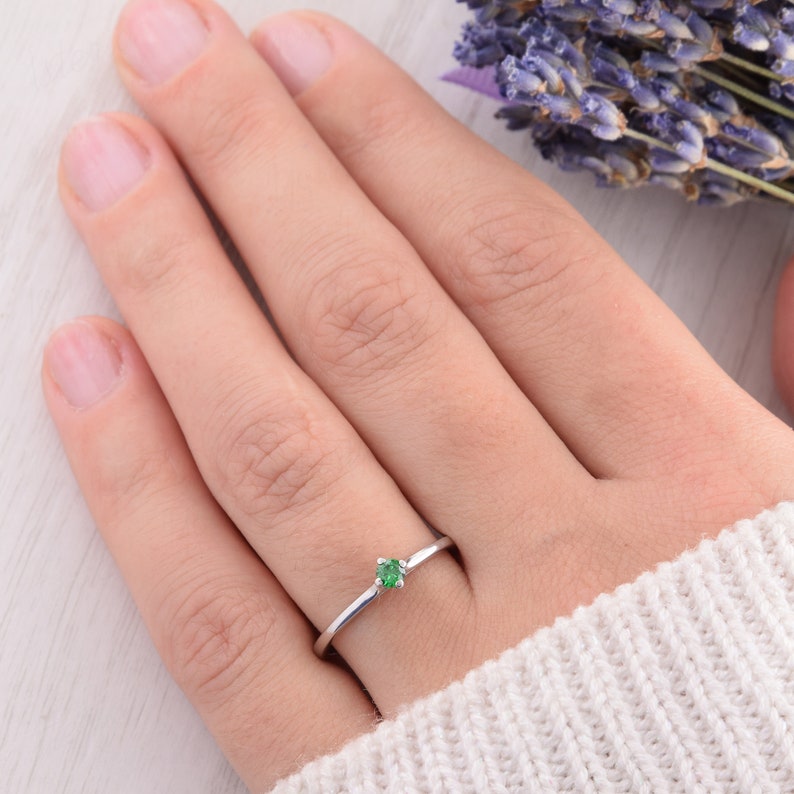 May include: A delicate silver ring with a small, round green gemstone set in the center.