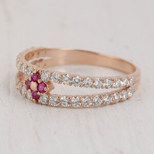 Puede incluir: Un anillo de oro rosa con una doble banda de piedras transparentes y un grupo central de piedras rosas.