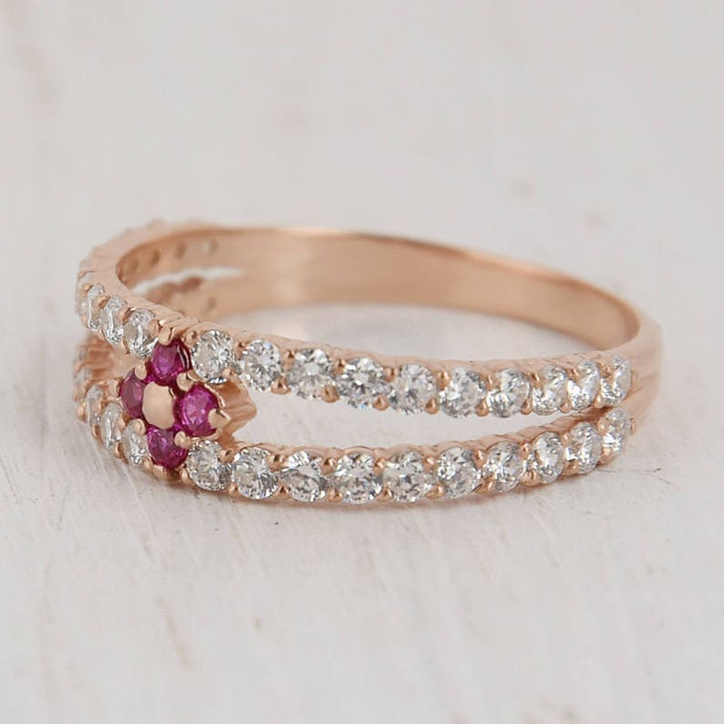 Puede incluir: Un anillo de oro rosa con una doble banda de piedras transparentes y un grupo central de piedras rosas.