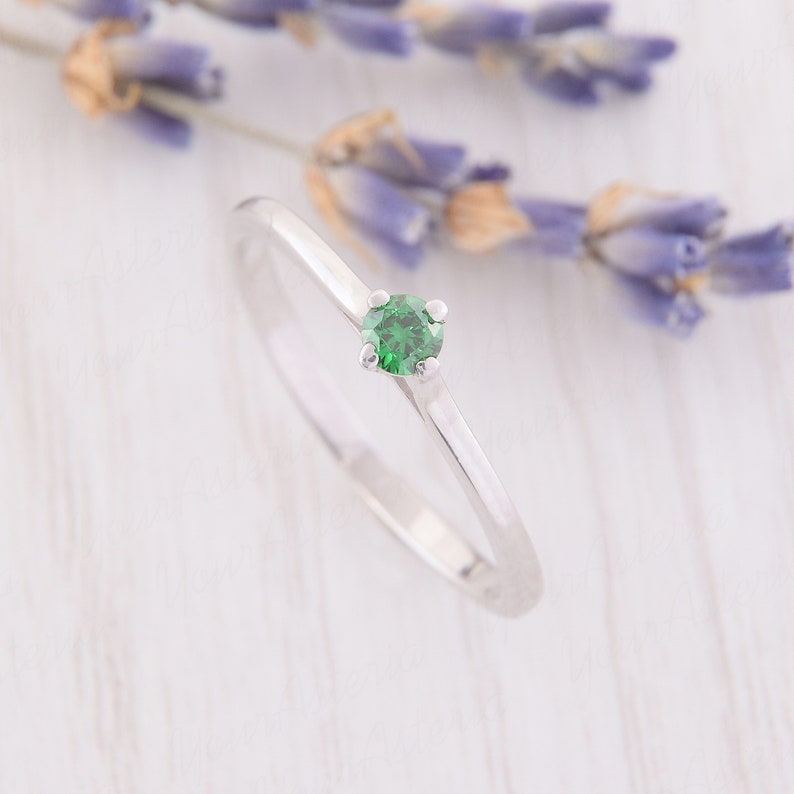 May include: A simple silver band ring with a small, round, green gemstone.