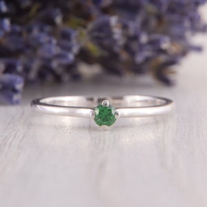 May include: A simple silver band ring with a single green gemstone in the center.