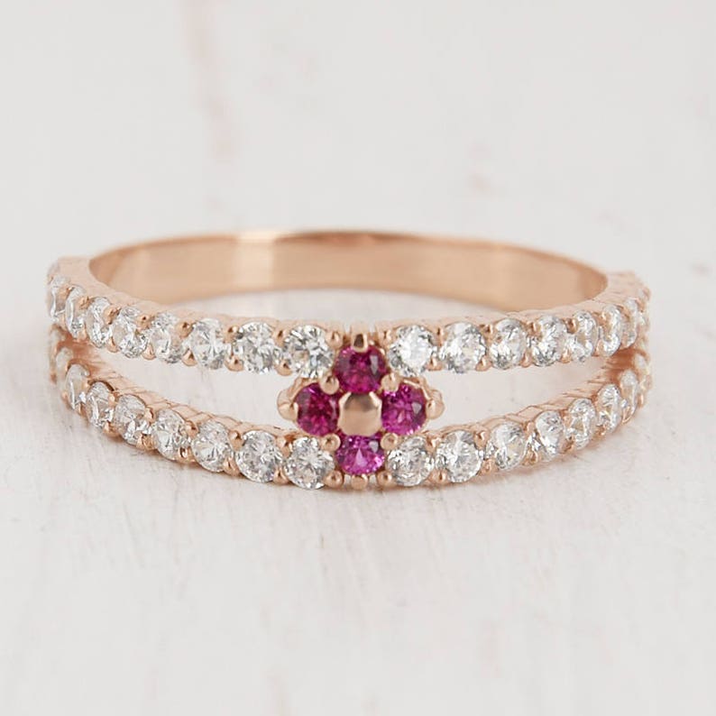 Puede incluir: Un anillo de oro rosa con una doble banda de peque&ntilde;as piedras transparentes y un grupo central de cinco piedras rosas.