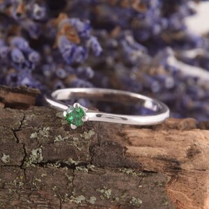 May include: A silver ring with a single green gemstone set in the center.
