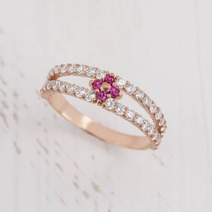 Puede incluir: Un delicado anillo de oro rosa con una doble banda de piedras blancas brillantes. Un peque&ntilde;o grupo de piedras rosas en forma de flor se encuentra en el centro del anillo.