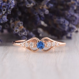 May include: A delicate rose gold ring with a blue sapphire center stone and smaller clear stones on the band.