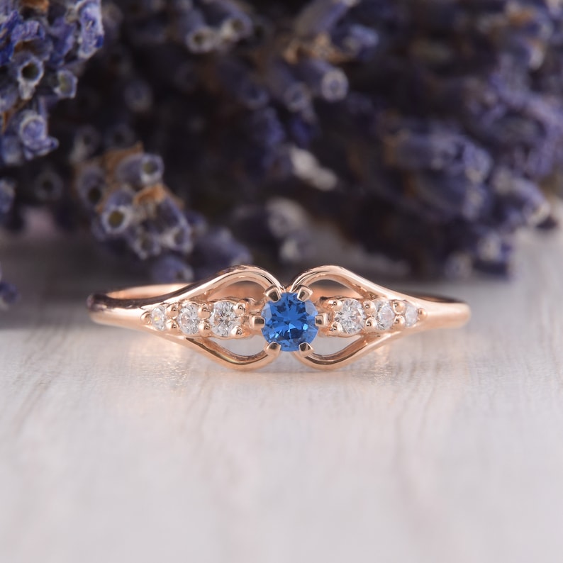 May include: A delicate rose gold ring with a blue sapphire center stone and smaller clear stones on the band.