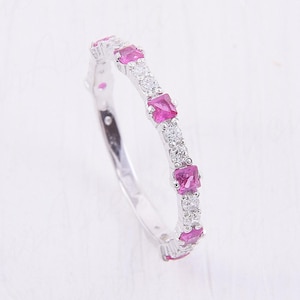 May include: A silver-toned band ring featuring an alternating pattern of square-cut vibrant pink stones and small, round, clear white stones set along the top half of the band. The metal has a polished, reflective finish throughout the entire ring.