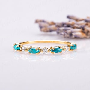 May include: A gold ring featuring an alternating pattern of marquise-cut turquoise stones and round-cut clear white stones set in a thin metal band. The design displays four turquoise stones and three clear stones arranged horizontally along the band.