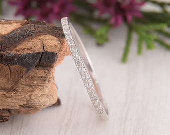 May include: A thin silver band with a row of small, clear diamonds set around the entire band.
