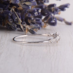 May include: A delicate silver band ring with a row of small, clear gemstones set in a curved design.