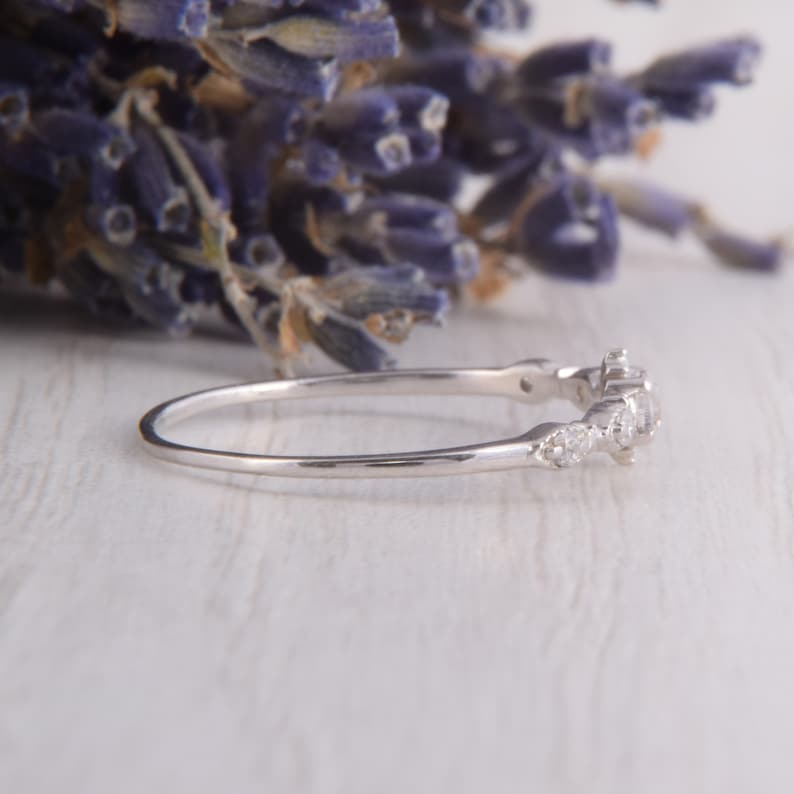May include: A delicate silver band ring with a row of small, clear gemstones set in a curved design.
