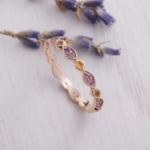 May include: A delicate gold band ring with a scalloped edge and a row of alternating purple and yellow gemstones.