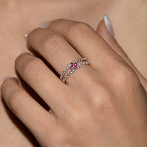 Puede incluir: Un delicado anillo con una doble banda de piedras transparentes y una flor central con piedras rosas.