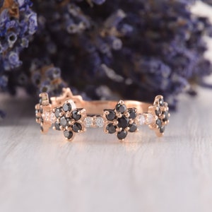 Op de afbeelding: Een delicate ros&eacute;gouden bandring met een bloemmotief. De ring heeft afwisselend zwarte en witte diamanten die in een bloemvorm zijn gezet.
