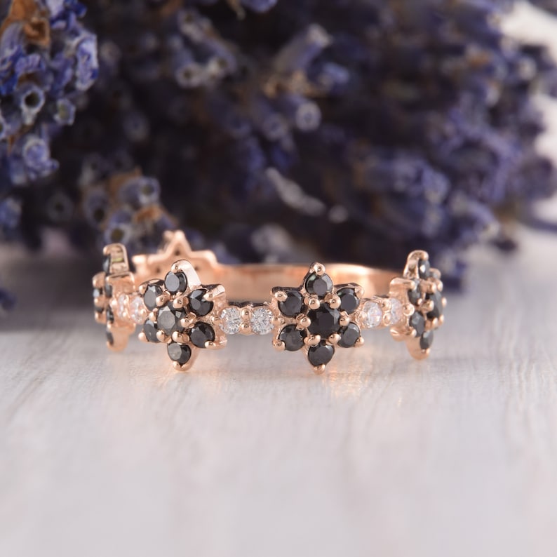 Op de afbeelding: Een delicate ros&eacute;gouden bandring met een bloemmotief. De ring heeft afwisselend zwarte en witte diamanten die in een bloemvorm zijn gezet.