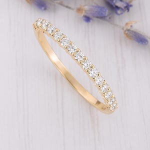 May include: A thin yellow gold band ring featuring a row of fourteen small, round, clear, faceted stones set along the top half of the band. The metal has a polished, reflective finish, and the stones are arranged in a continuous, uniform line.