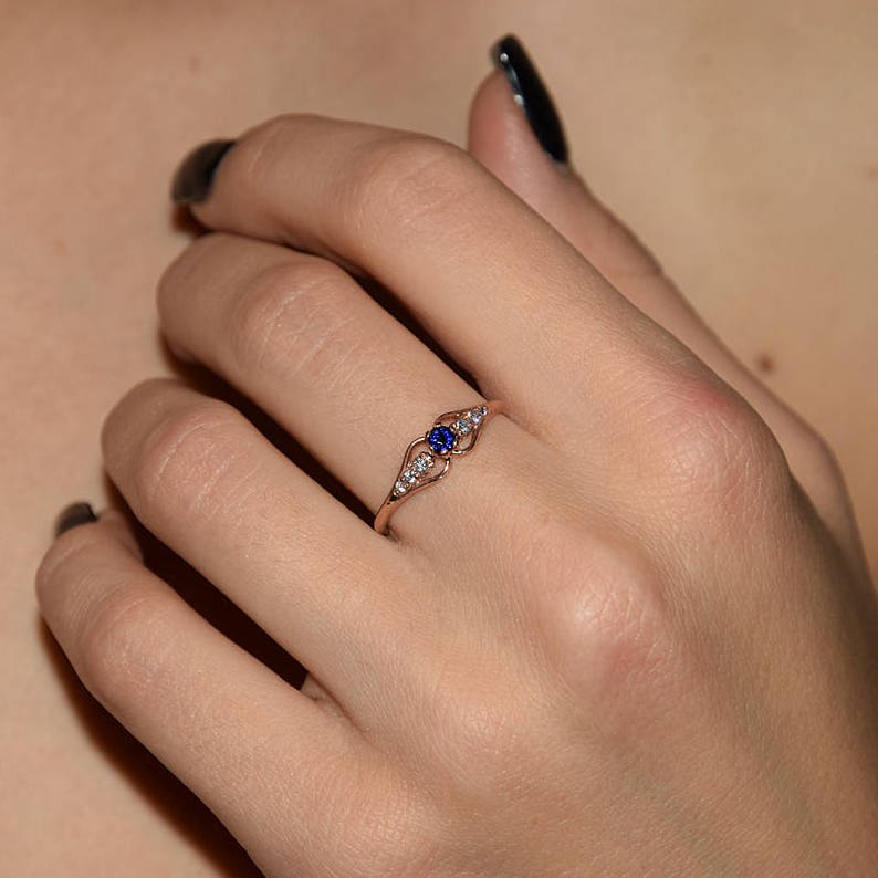 May include: A delicate rose gold ring with a blue sapphire and small clear diamonds set in a heart-shaped design.