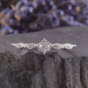 May include: A delicate silver ring with a single round-cut diamond in the center and smaller diamonds on each side. The ring has a vintage-inspired design.