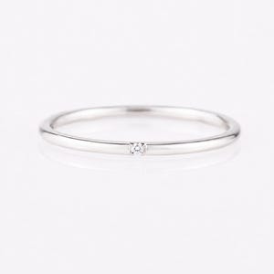 Può includere: Un sottile anello in metallo color argento lucido con una singola piccola pietra preziosa trasparente a taglio rotondo, incastonata a filo al centro della fascia. L'anello presenta un profilo liscio e arrotondato con una finitura metallica.