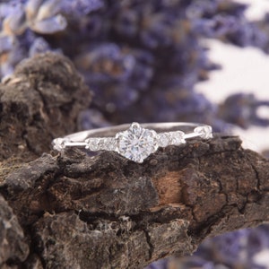 May include: A delicate silver ring with a single, round, clear diamond in the center and smaller diamonds on the band.