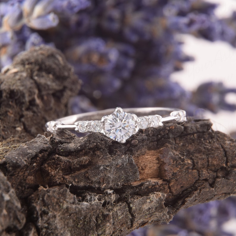 May include: A delicate silver ring with a single, round, clear diamond in the center and smaller diamonds on the band.