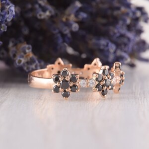 Op de afbeelding: Een ros&eacute;gouden bandring met drie zwarte diamantbloemmotieven. De ring is bezet met kleine witte diamanten tussen de bloemen.