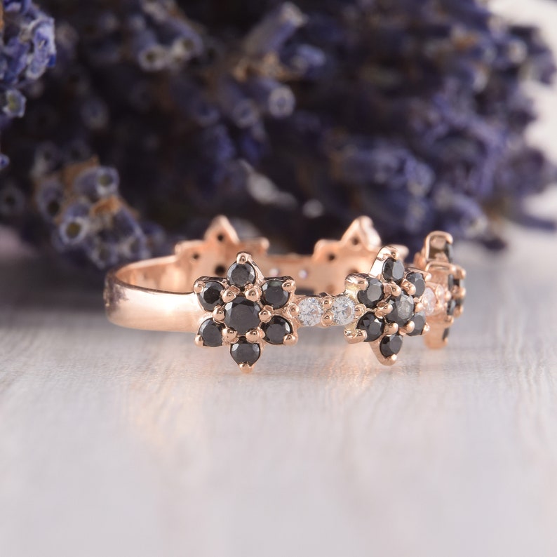 Op de afbeelding: Een ros&eacute;gouden bandring met drie zwarte diamantbloemmotieven. De ring is bezet met kleine witte diamanten tussen de bloemen.
