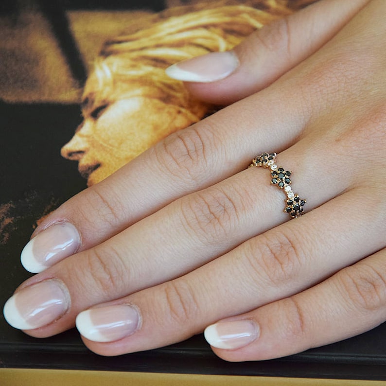 Op de afbeelding: Een gouden ring met een rij zwarte diamanten in een bloemvorm.