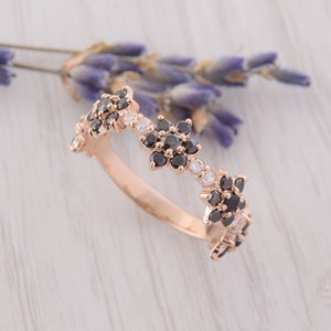 Op de afbeelding: Een ring van ros&eacute;goud met een delicaat bloemenmotief. De ring is bezet met zwarte en witte edelstenen die in een bloemenpatroon zijn gerangschikt.