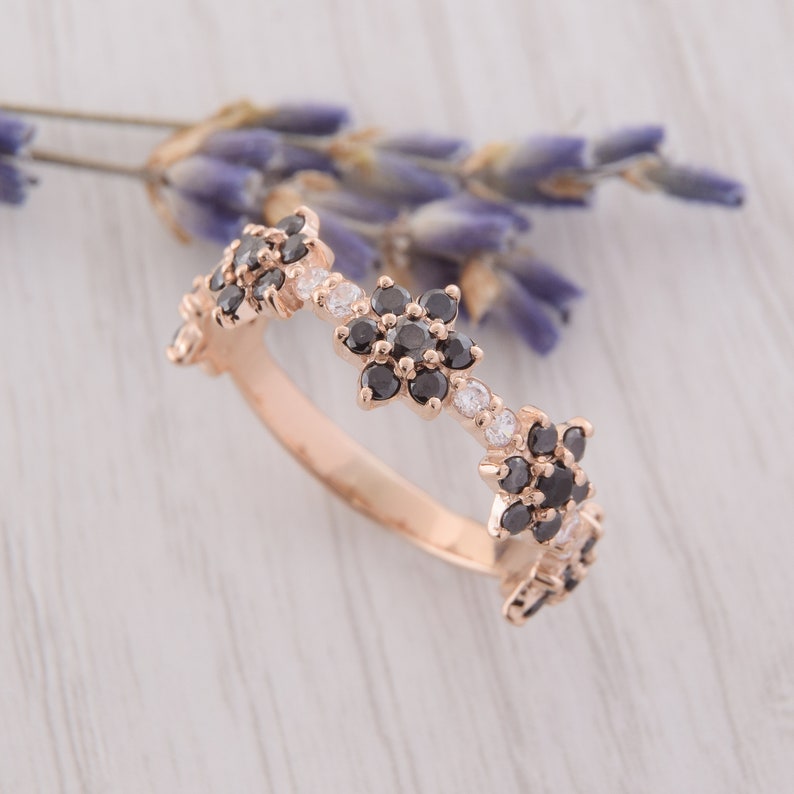 Op de afbeelding: Een ring van ros&eacute;goud met een delicaat bloemenmotief. De ring is bezet met zwarte en witte edelstenen die in een bloemenpatroon zijn gerangschikt.