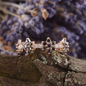 Op de afbeelding: Een ring van ros&eacute;goud met een delicaat bloemmotief. De ring is bezet met zwarte en witte diamanten.