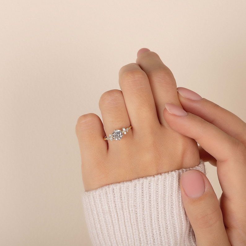 K&ouml;nnte beinhalten: Ein goldener Ring mit einem gro&szlig;en runden Mittelst&uuml;ck und kleineren Steinen auf beiden Seiten. Der Ring befindet sich an einem Finger.