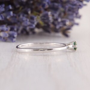 May include: A silver ring with a single green gemstone set in a prong setting.