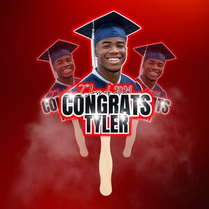 May include: A graduation fan featuring a smiling young man in a cap and gown. The fan reads "Congrats Tyler" with "Class of 2024" above. The background is a gradient of red.