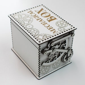 May include: A white wooden mechanical box with intricate gear and lever designs on the side. The top of the box features the words "MECHANICAL BOX" in gold lettering, surrounded by decorative gear patterns. The box is a unique storage item.